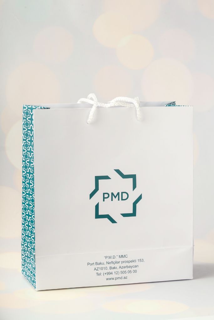 PMD MMC gift bag — white coated board, teal side pattern, white rope handle, PMD logo, Port Baku address