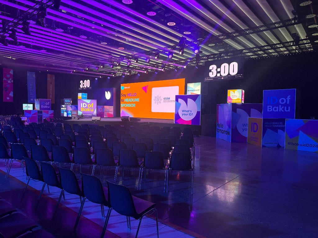 Baku ID 2024 stage wide view — purple lighting, LED wall with branded sponsor cubes