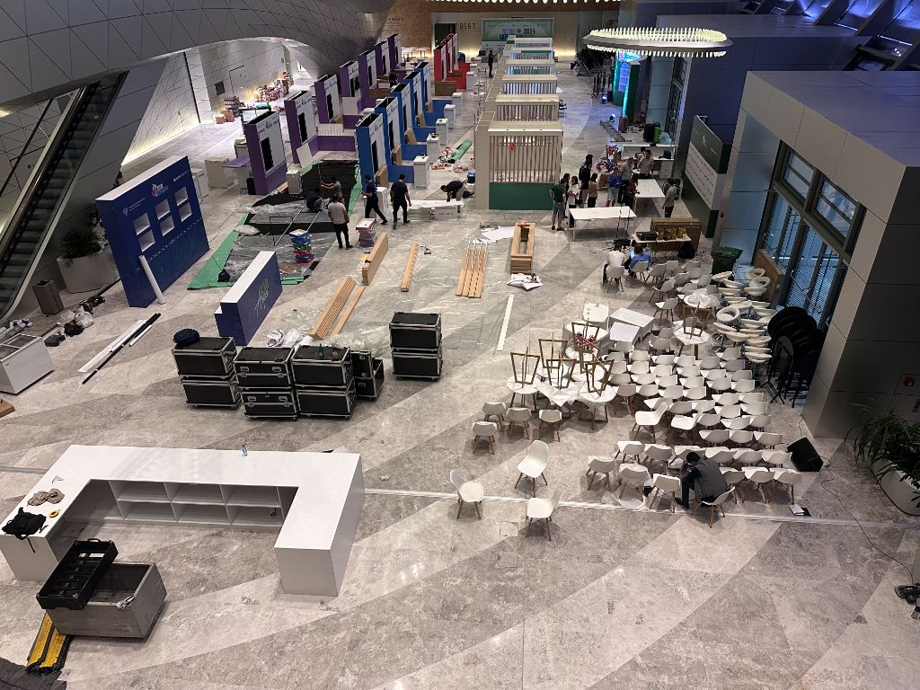 Construction phase — workers assembling pavilions with chairs and equipment scattered on floor
